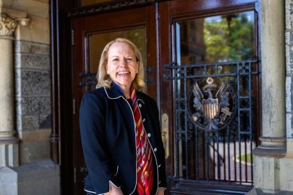 A woman in a navy blazer stands outside doors