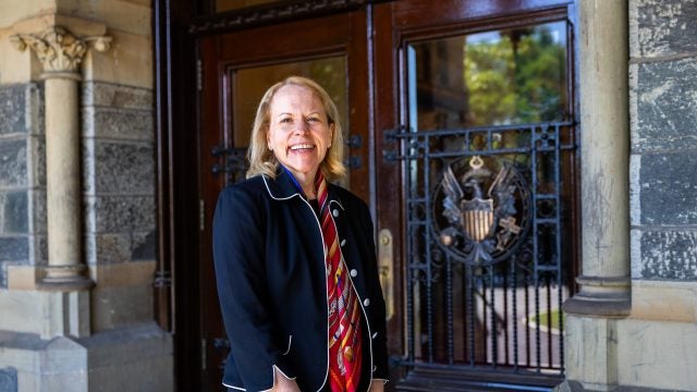 A woman in a navy blazer stands outside doors