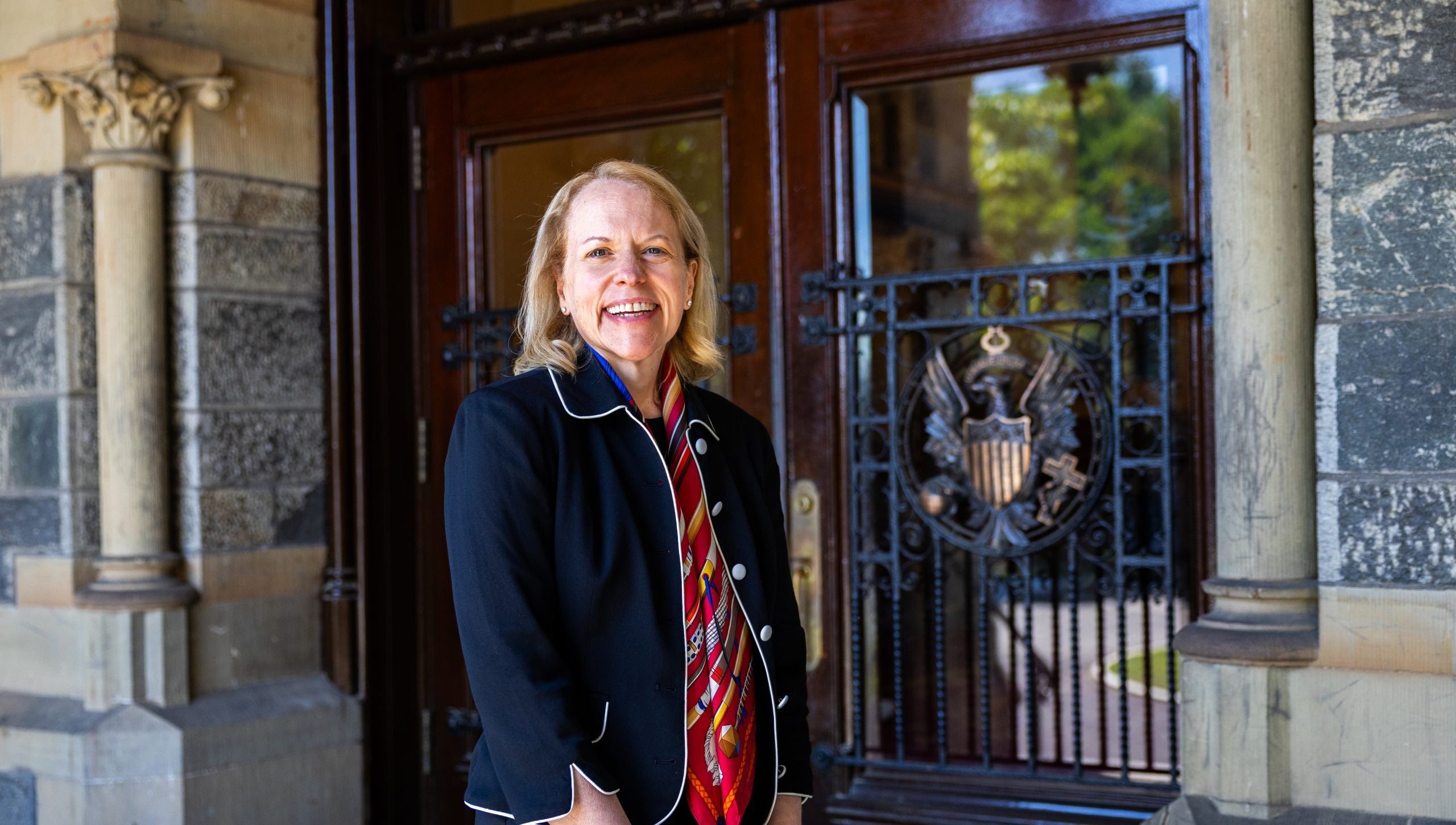 A woman in a navy blazer stands outside doors