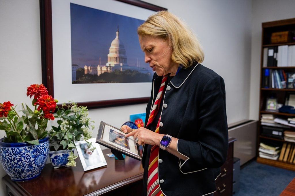 A woman in a navy blazer points to a framed photo of herself in her office