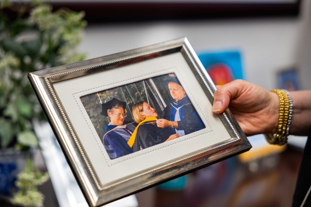 A woman holds a frame of a photo of her graduating from college.