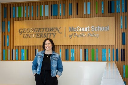 A woman in a jean jacket stands in front of a sign that says "Georgetown University McCourt School of Public Policy"