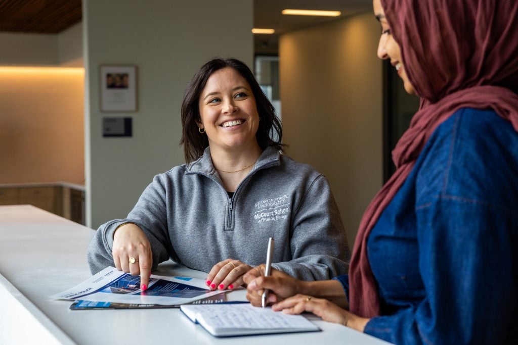A woman smiles while pointing to a brochure and talking to a student