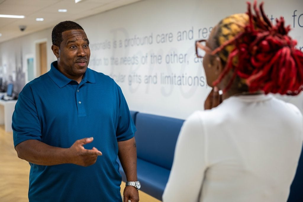 Black man in blue shirt walking talking to a Black woman inside