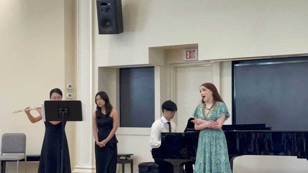Young woman in blue dress sings with three other musicians behind her