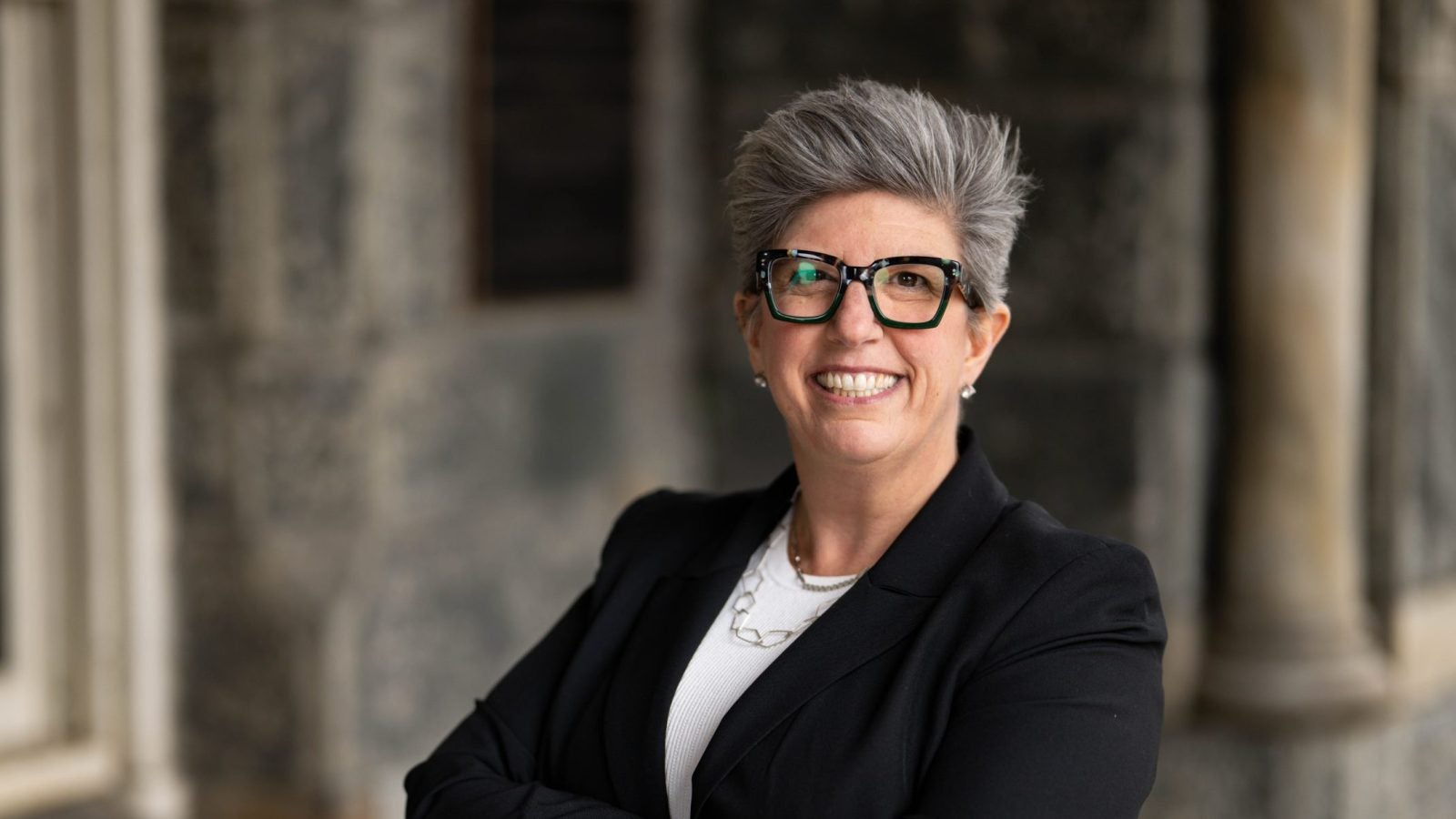 Woman with gray hair and glasses in business attire smiling with arms crossed