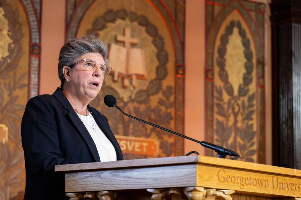 Woman in blazer with glasses and gray hair speaks at a podium in Gaston Hall