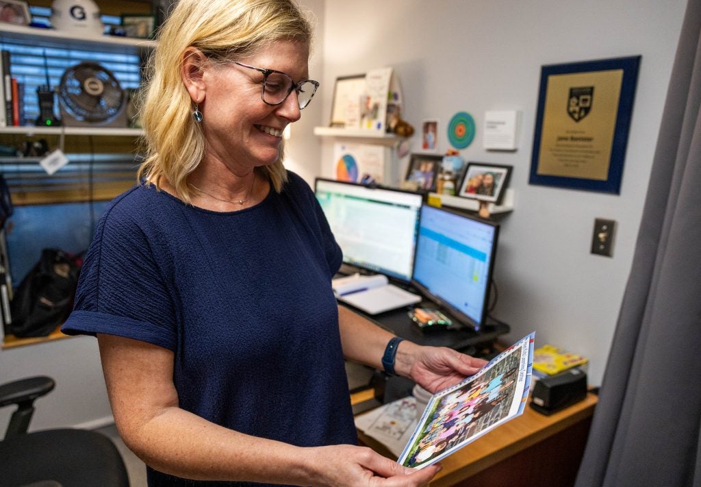 A blonde-haired woman in a navy shirt smiles while looking at a photo