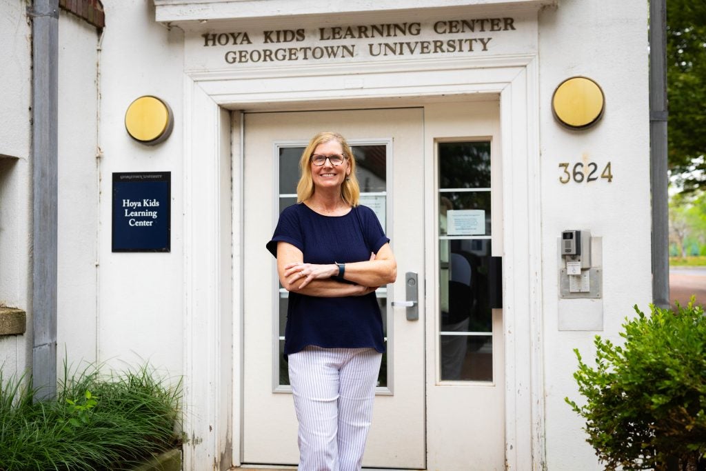 A woman smiles in front of a white building that says Hoya Kids Learning Center above the door