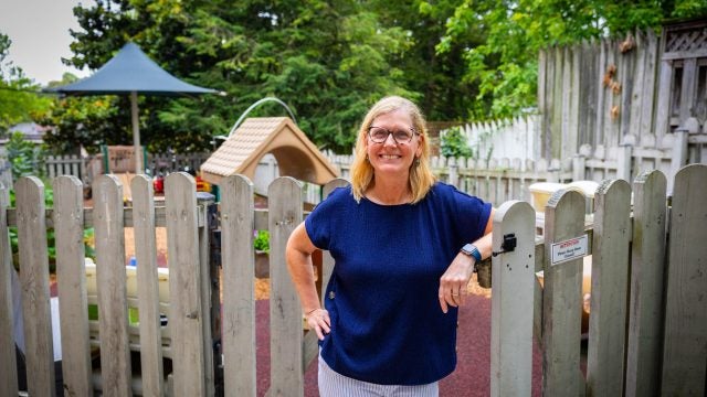 A woman in a navy shirt leans on a fence with a playground behind her