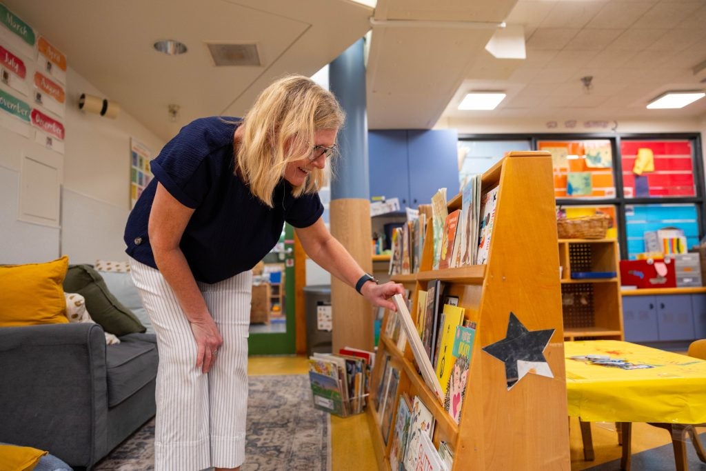 A woman picks up books out of a shelf 