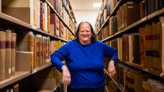 A woman in a bright blue shirt poses in between shelves of archival records