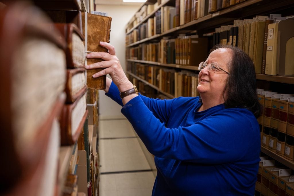 A woman in a bright blue shirt takes a file off a shelf