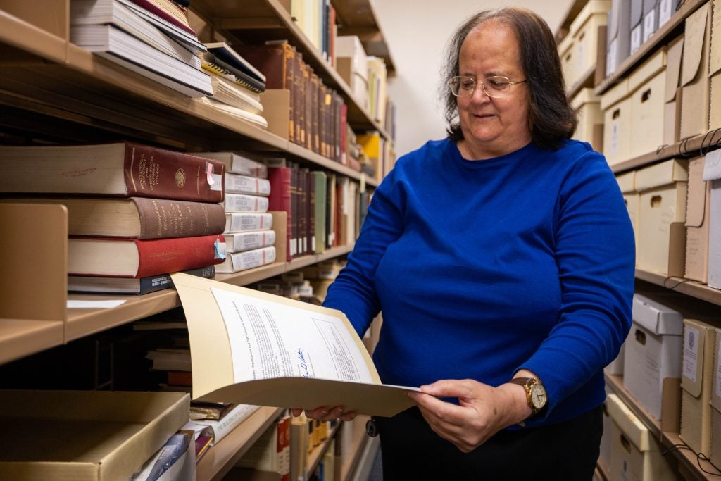 A woman in a bright blue shirt opens a manila folder in a library