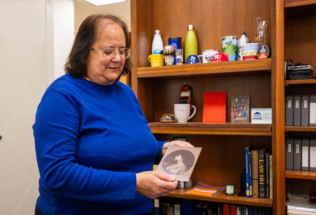 A woman holds up a portrait in front of a bookshelf