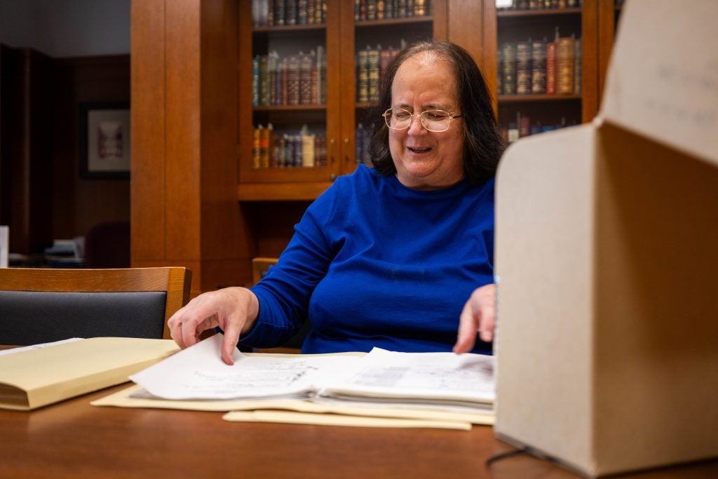 A woman in a bright blue shirt smiles while looking at a folder on a desk