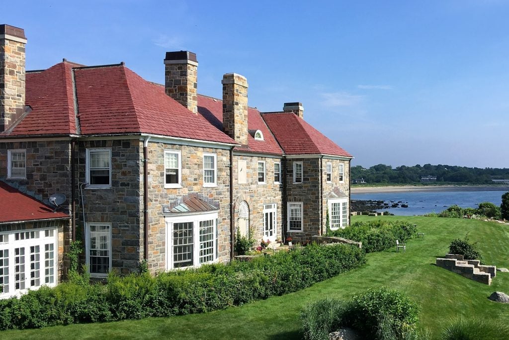 A stone mansion overlooking a green lawn and ocean