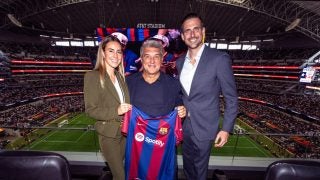 Woman with two men holding up a soccer jersey in a stadium