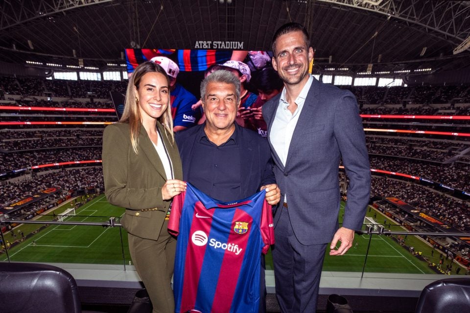 Woman with two men holding up a soccer jersey in a stadium