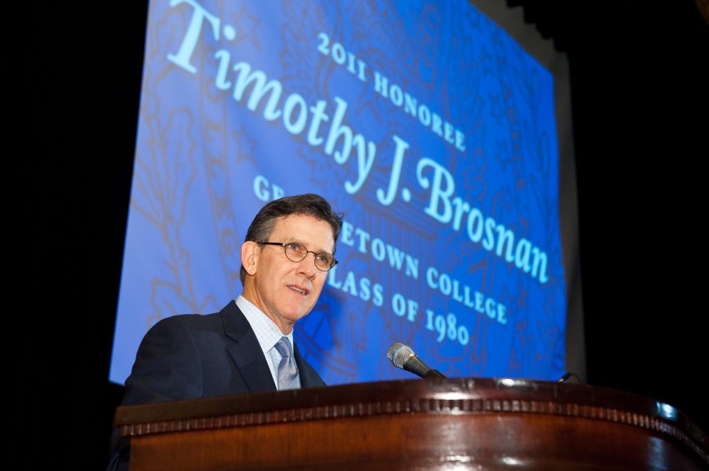 Tim Brosnan in suit and tie speaking at a podium on stage