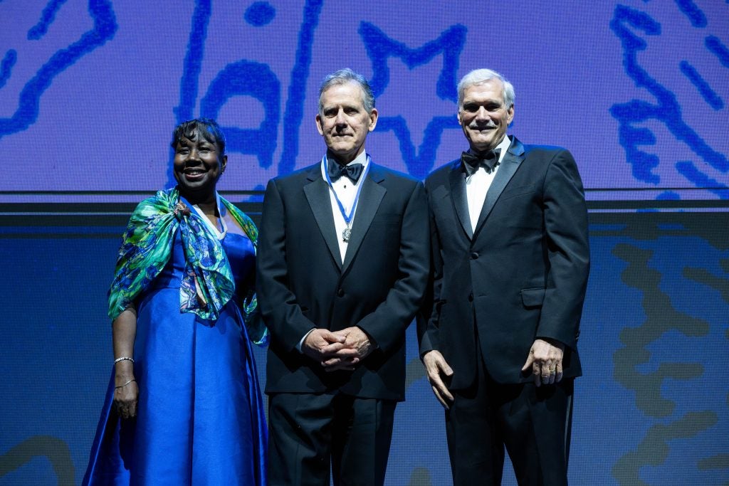 Two men in suits and bow ties with a woman on stage