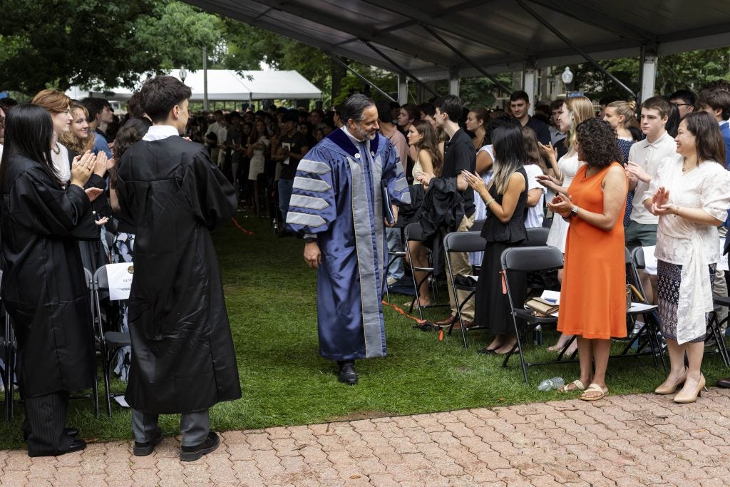 Eduardo Peñalver walking across Copley lawn in academic regalia