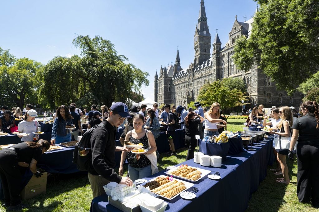 Students get food from a bbq on Copley Lawn on a sunny day with Healy Hall in background