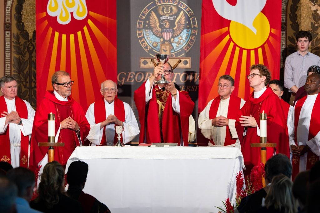 A Catholic priest in red vestments holding a chalice during a Catholic Mass