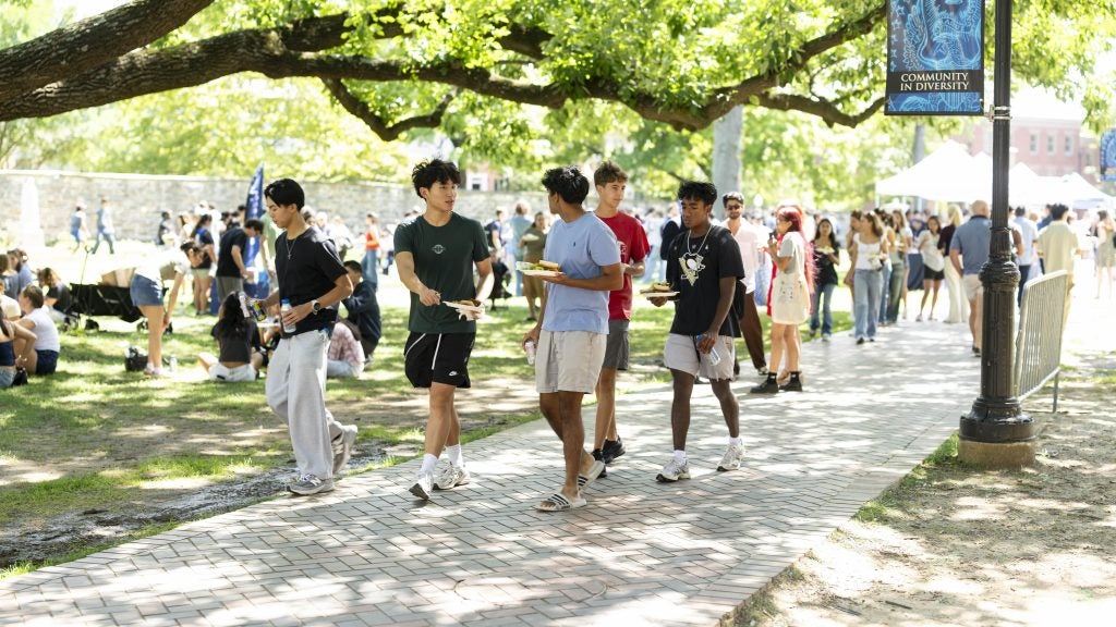 Students walk along a path with plates from a bbq on Copley Lawn on sunny day