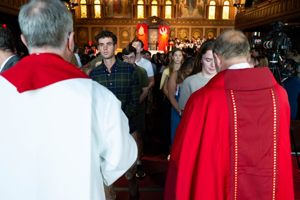 Two priests in red vestments distributing communion in Gaston Hall
