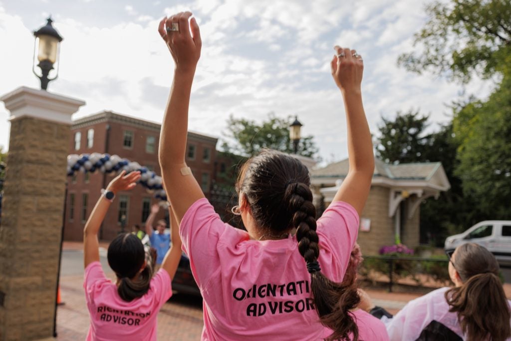 Young woman with arms raised wearing a pink orientation advisor shirt