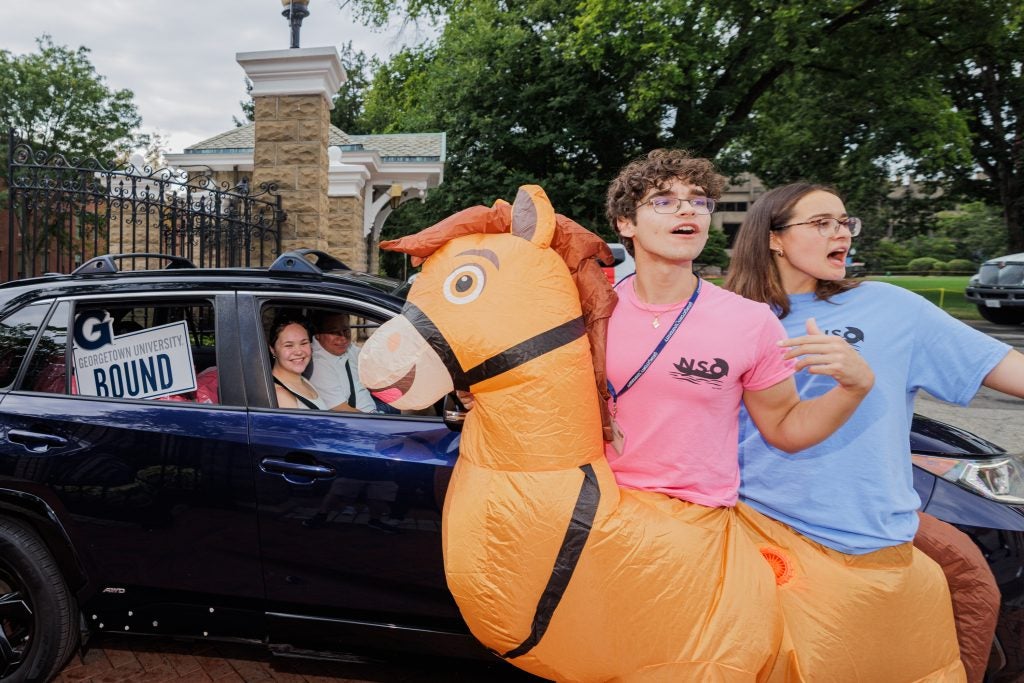 Two students in a horse inflatable costume excited as a car with a new student arrives