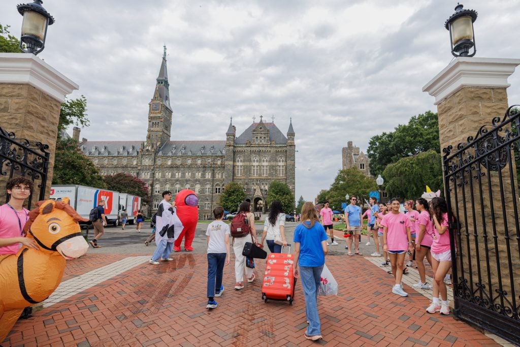Students rolling through Healy gate with suitcases on a cloudy day