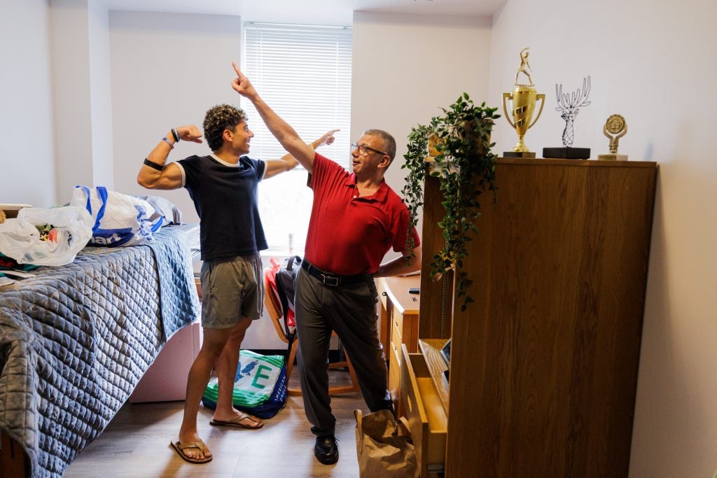 Young man and his dad raise their arms in a dorm room