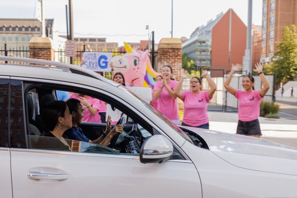 A car pulls up as Hoyas in pink shirts cheer them on