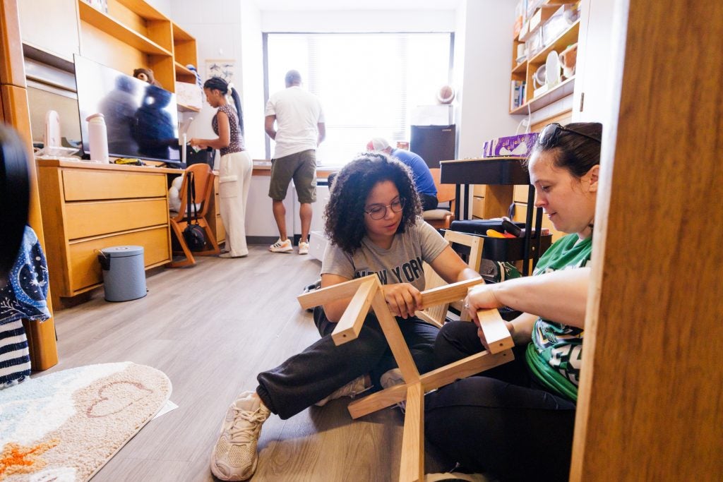 Two young women build furniture in a dorm room