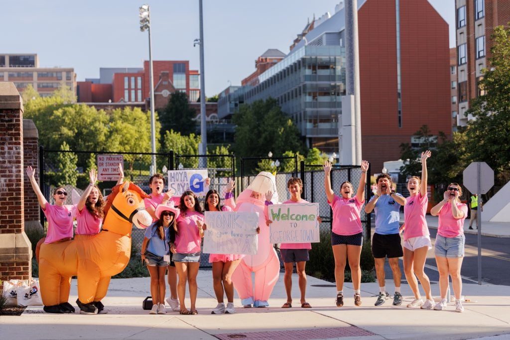 Hoyas in pink orientation advisor shirts cheer and smile on a sunny day