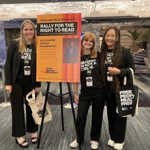 Three female students pose beside a sign advertising a movie