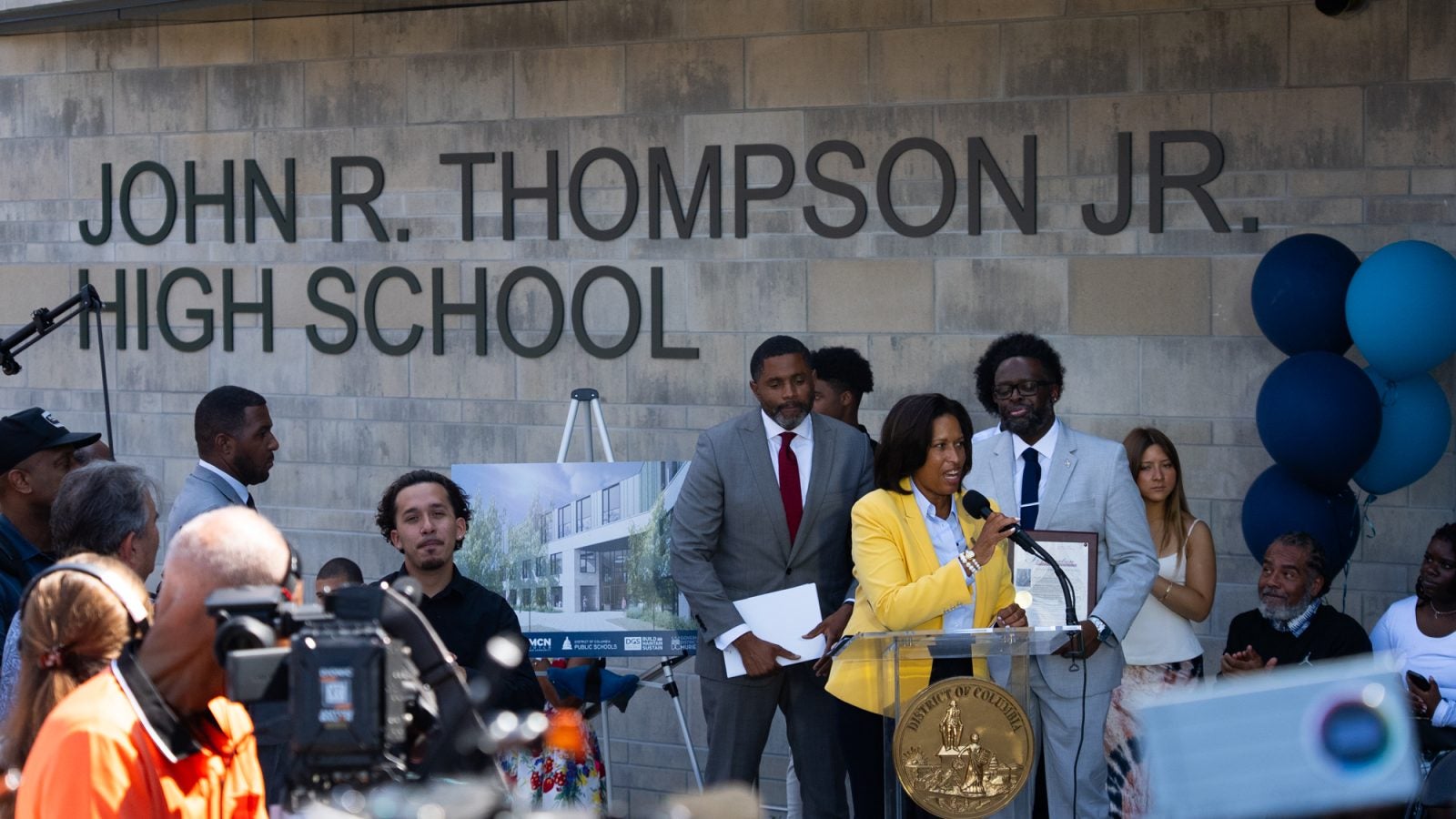 People gathered in front of John R. Thompson High School as a Black woman speaks at a podium