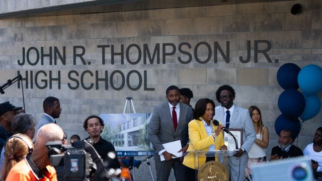 People gathered in front of John R. Thompson High School as a Black woman speaks at a podium