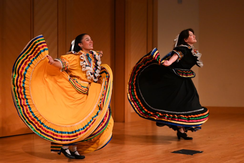 Two students in traditional Mexican dress dance on a stage