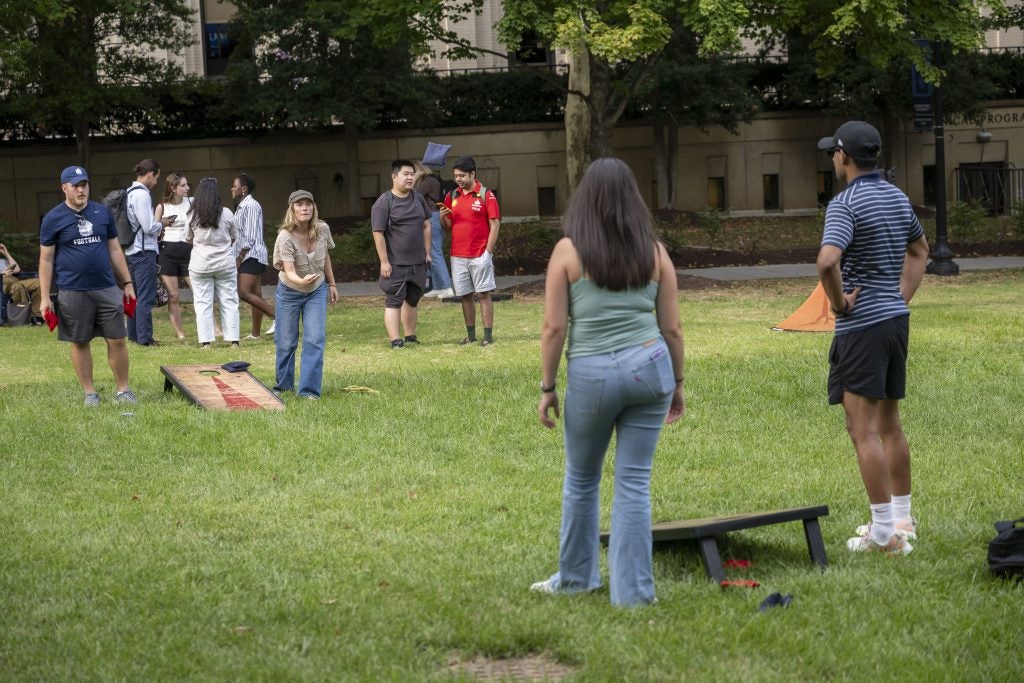 Students playing cornhole on a lawn
