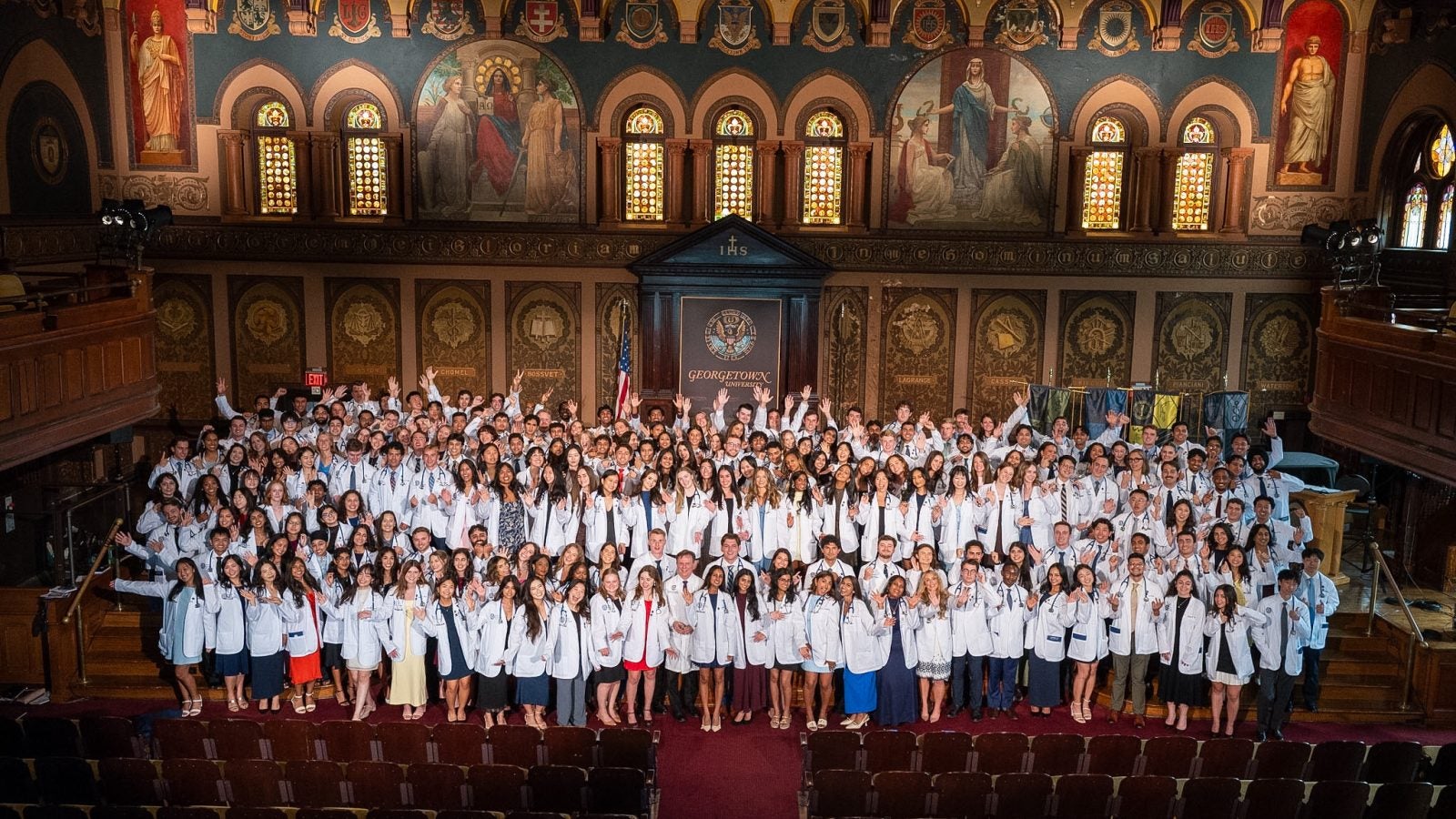 A group shot of medical students wearing white coats on a stage