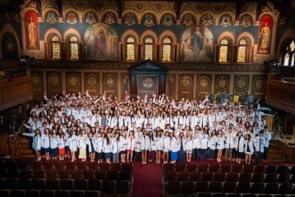 A group shot of medical students wearing white coats on a stage