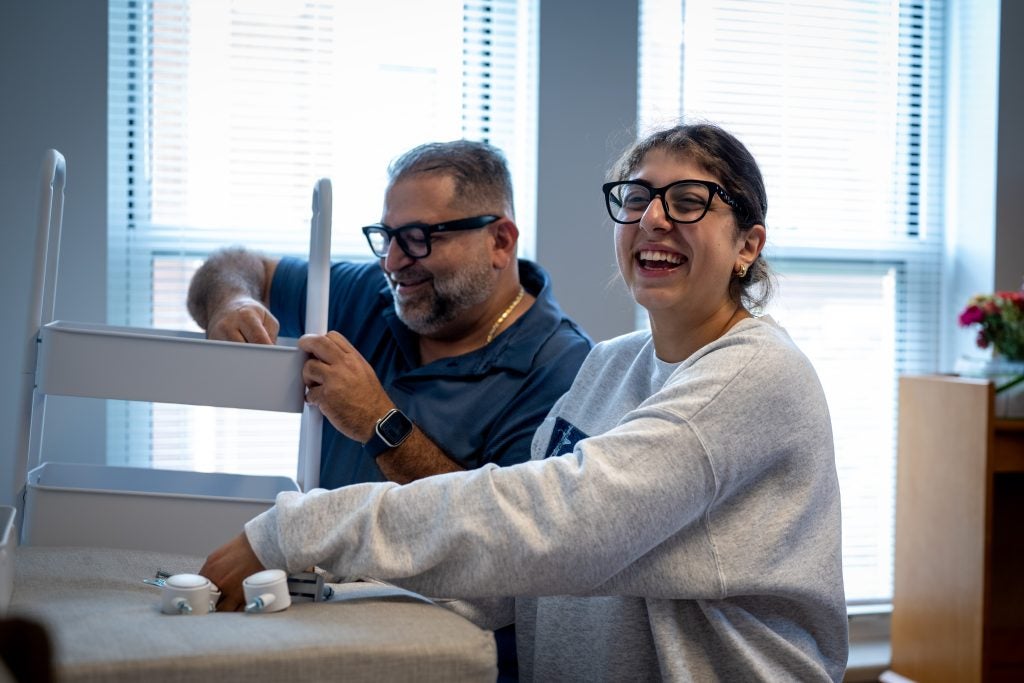 Young woman and her dad smiling while assembling furniture in dorm