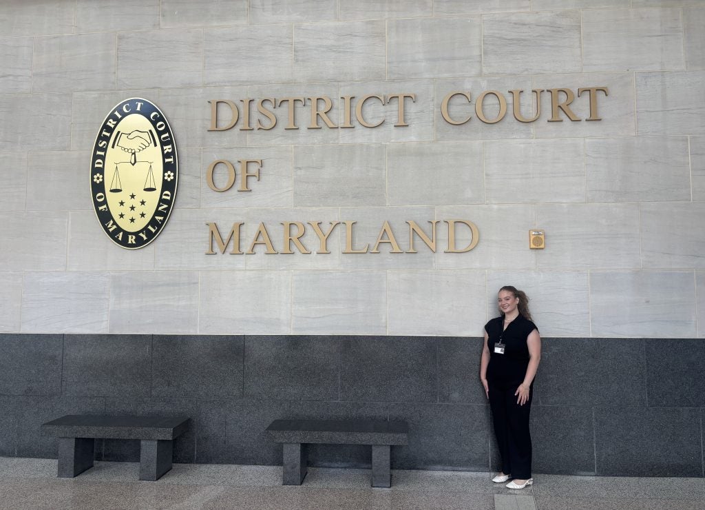 A student poses in front of text on a wall that says District Court of Maryland