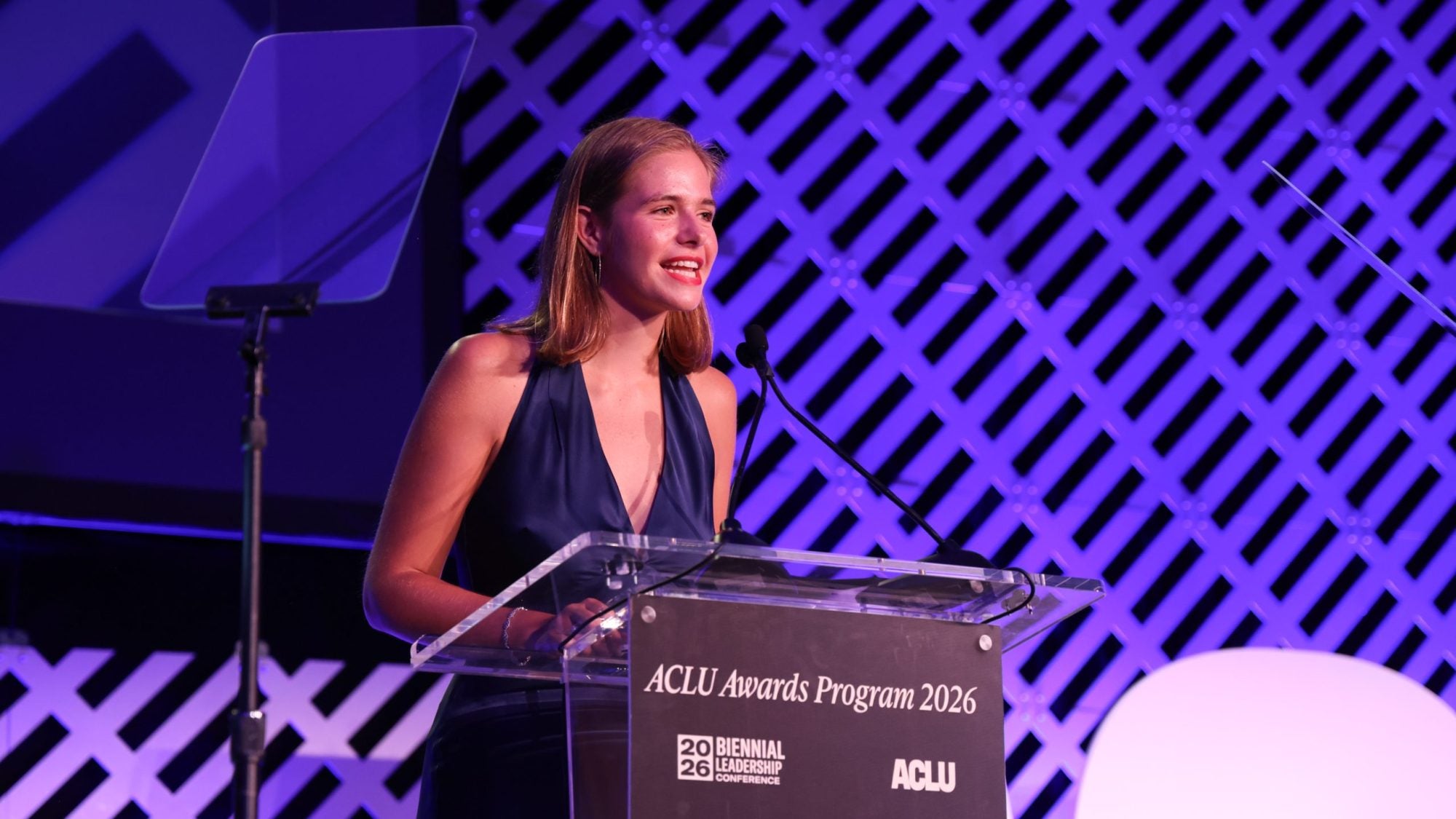 A student in an evening gown speaks from behind a lectern