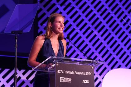 A student in an evening gown speaks from behind a lectern