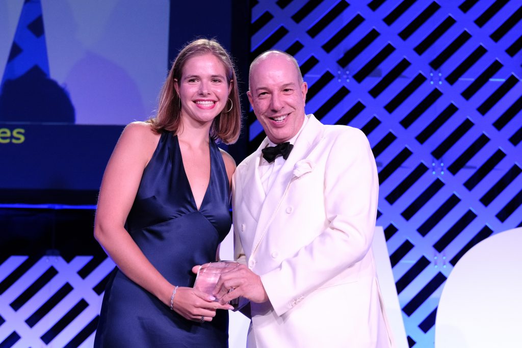 A female student in a navy dress poses with a man while receiving an award onstage