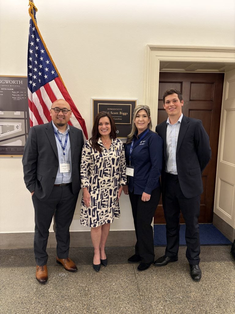 Two men and two women outside a congressional office with American flag